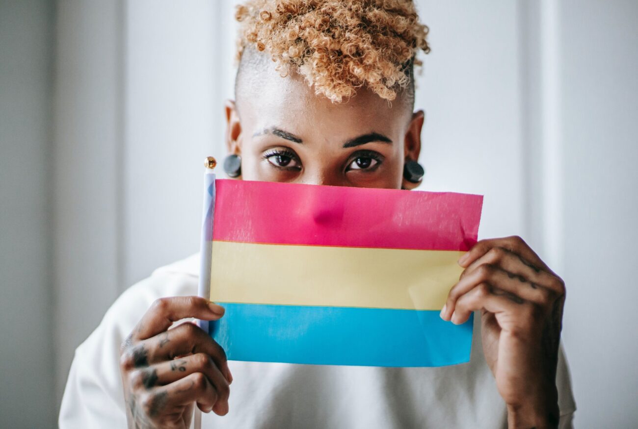A young black person holding a pansexual flag half concealing their face.